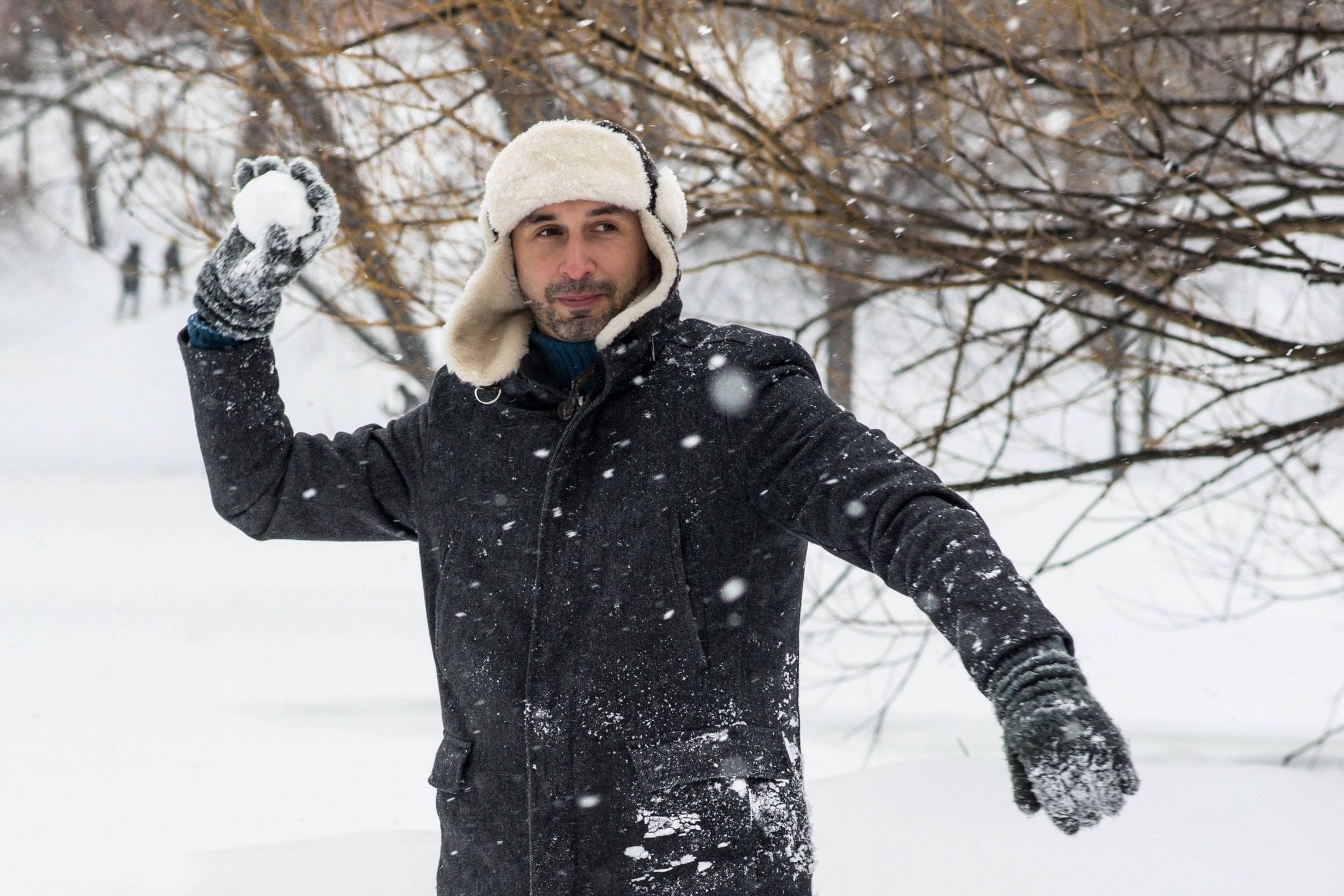 A man in extreme winter conditions, wrapped up in a coat, throwing a snowball