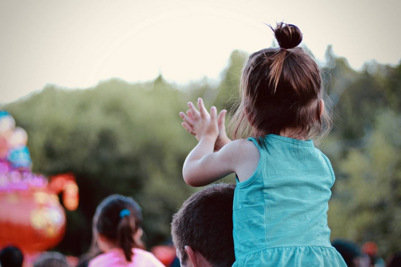 Girl toddler on a man's shoulders claps her hands in congratulations
