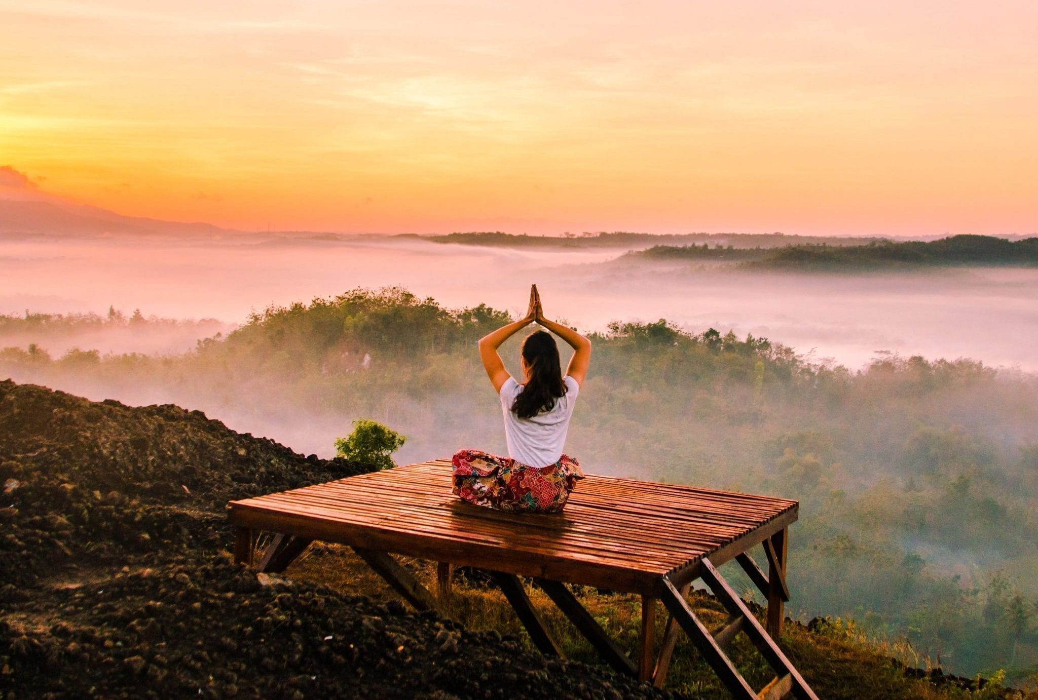 Girl meditating a wooden platform in front of a beautiful scenery 