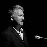  James Kerr in a black and white setting with a microphone before him 