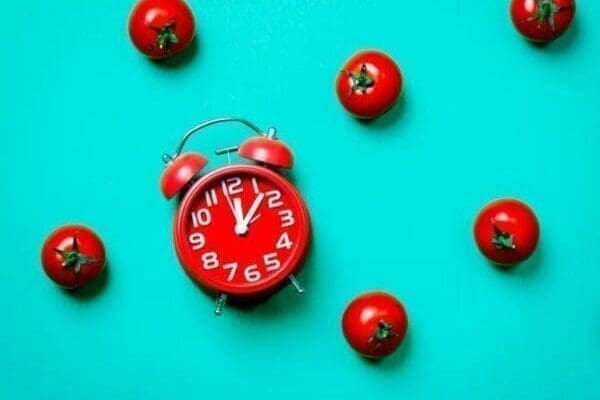 Tomatoes and alarm clock for Pomodoro Technique on blue background