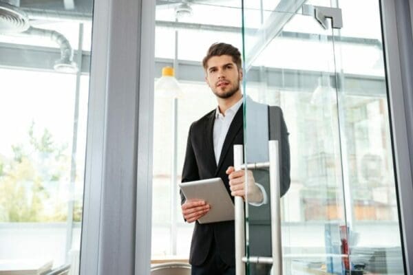 Businesman with tablet entering the door in office knows how to talk to anyone